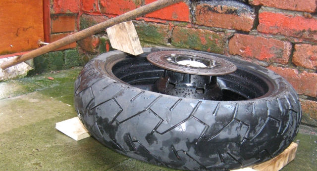 motorcycle tyre and wheel with long bar and block of wood to break tyre bead